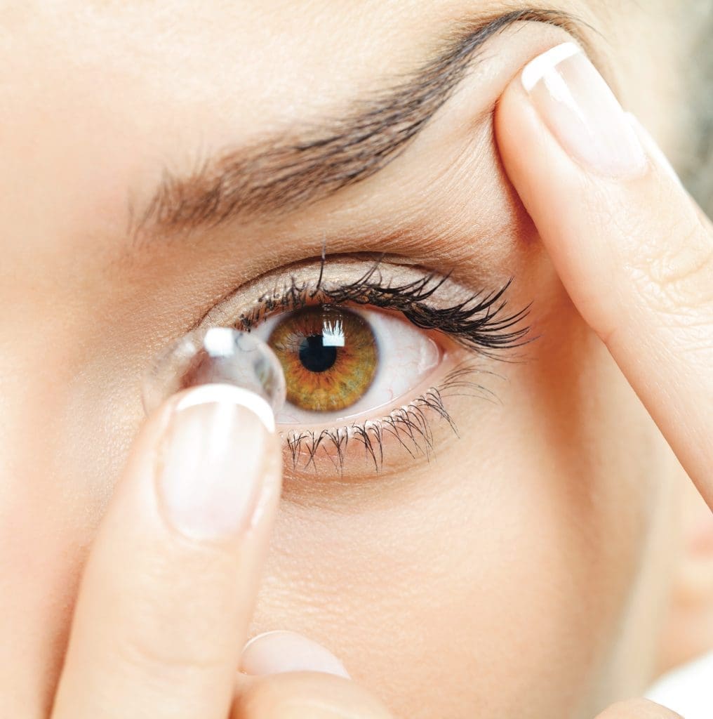 Young woman inserting a contact lens into her eye. Macro studio shot.