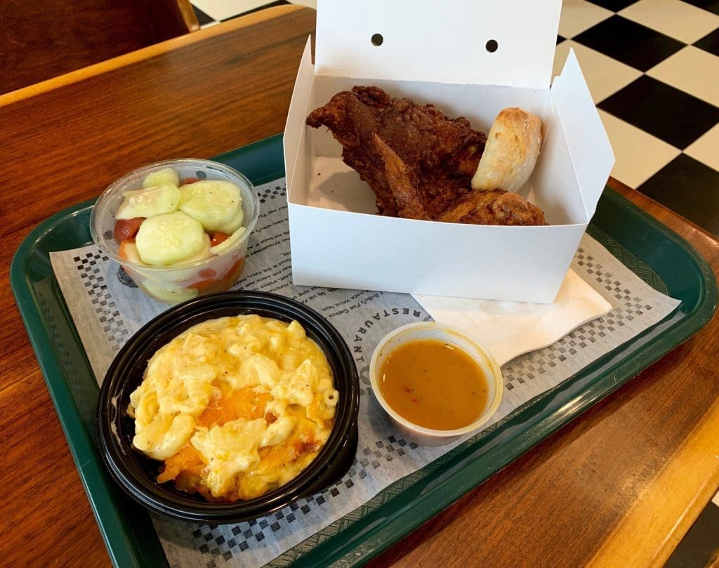 Fried chicken, a biscuit, mac and cheese, cucumber salad and gravy in a takeout box on a green tray.